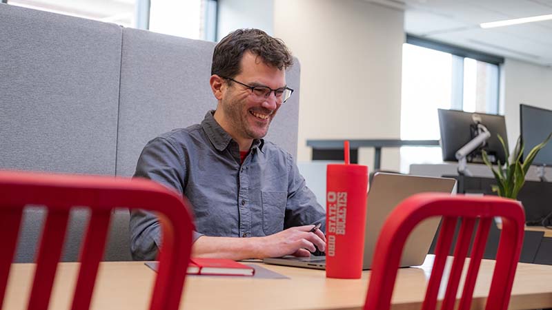 Smiling man at a table looking at his laptop